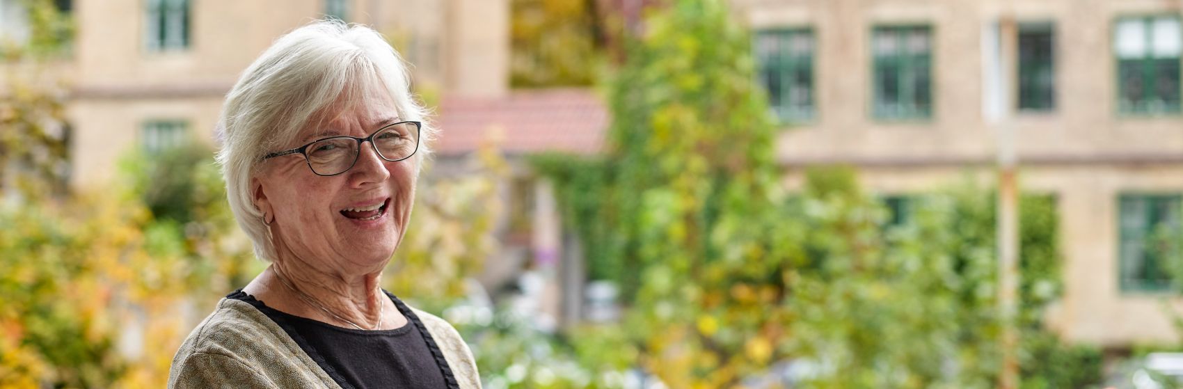 En eldre kvinne smiler til kameraet, hun står utenfor inngangen til Gabels Park.