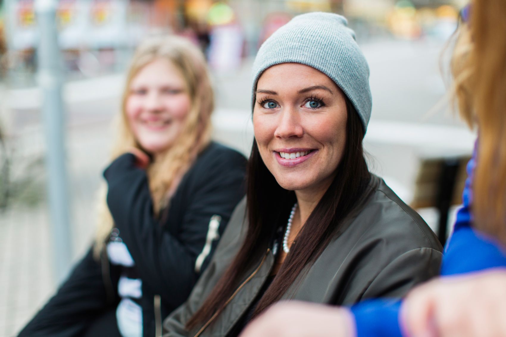 En smilende kvinne, i bakgrunn sitter en tenåringsjente