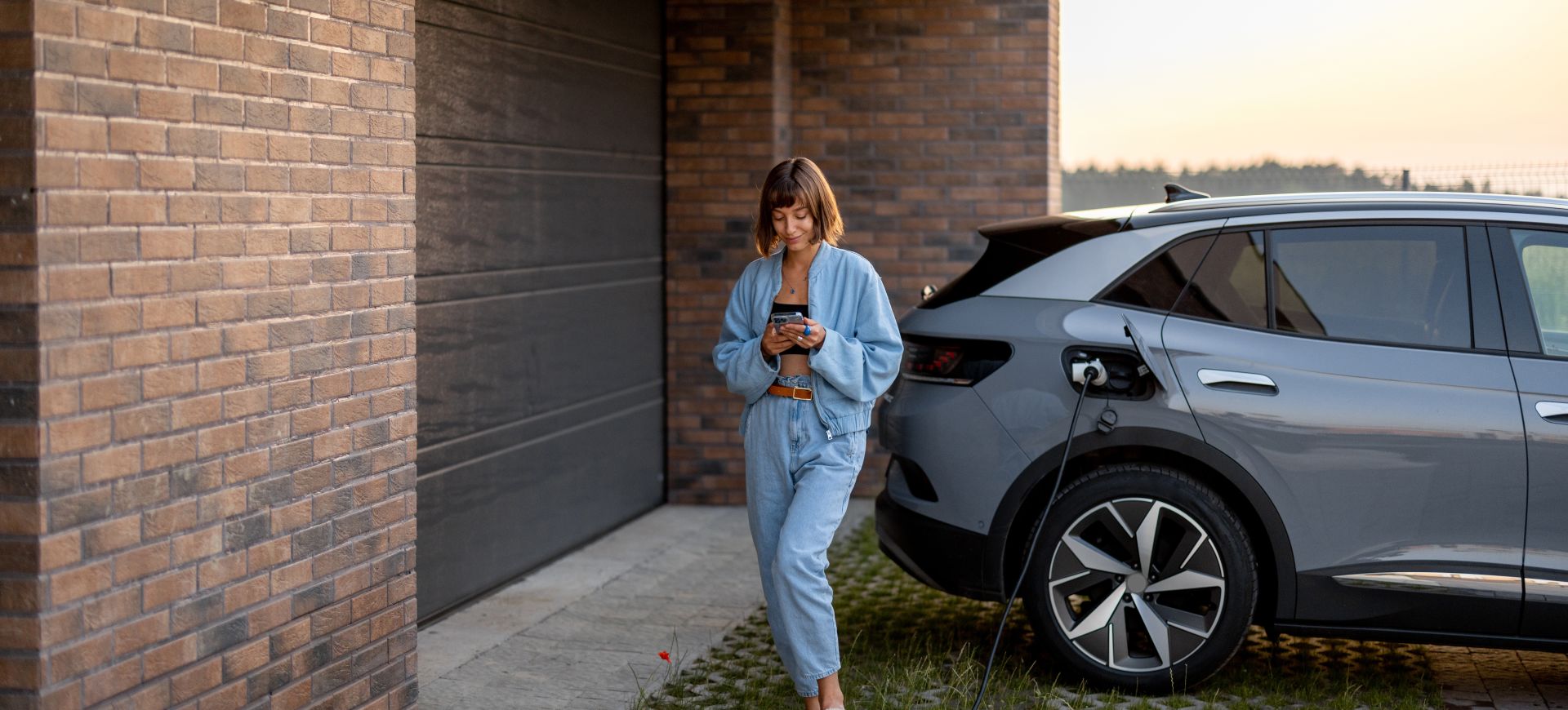 En ung dame som lader elbilen sin og sjekker lading via mobilen sin