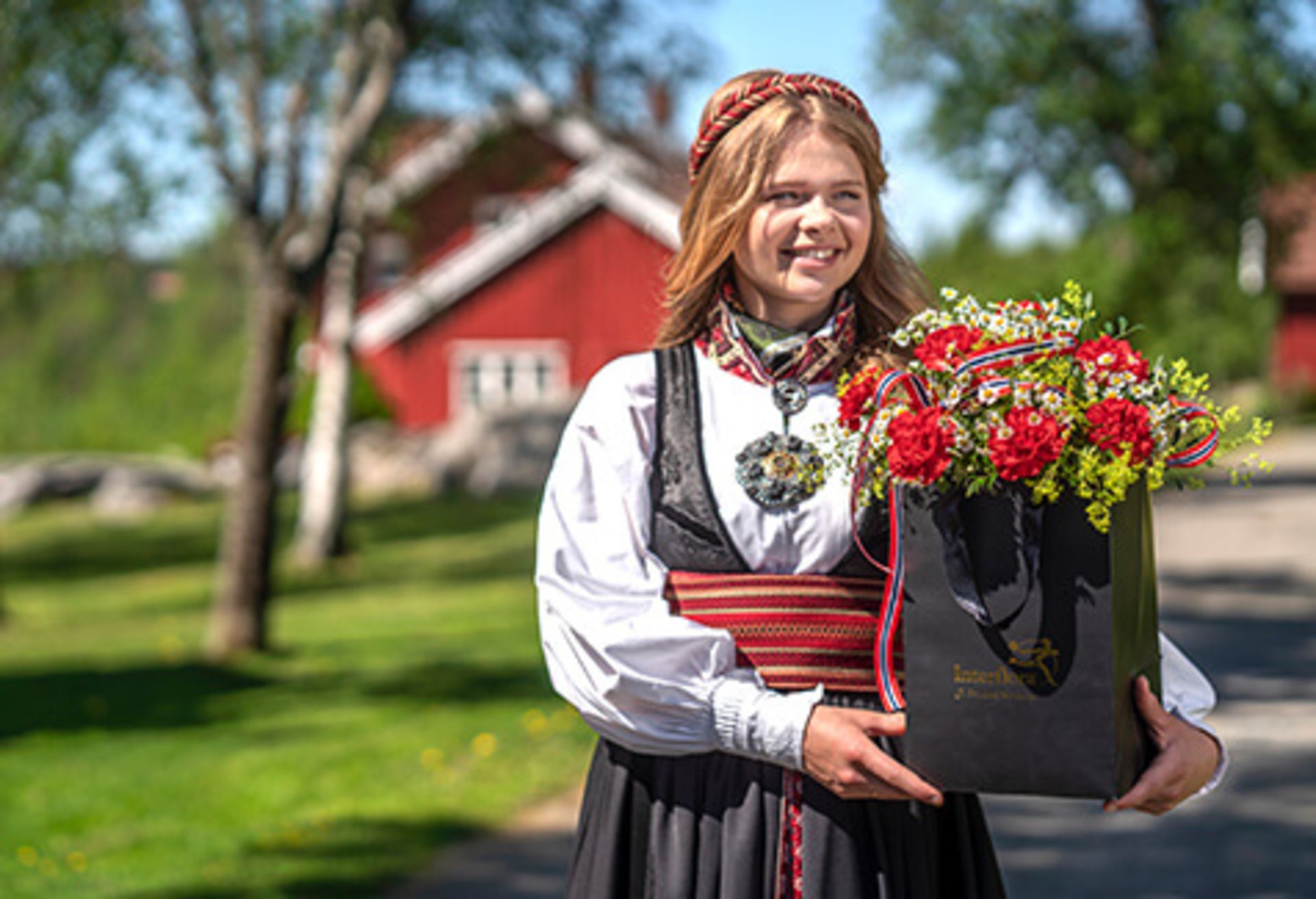 Kvinne i bunad med en blomstrende 17. mai-hilsen fra Interflora