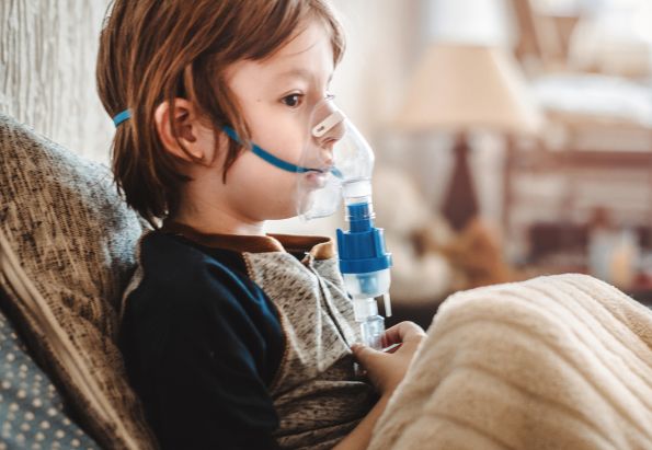 En ung gutt sitter i sofaen med en pustemaske over nese og munn.