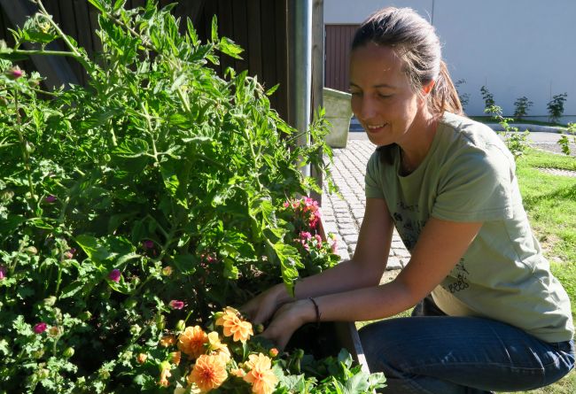 Bydelsmor Frøydis sitter på huk på en gressplen foran et blomsterbed.