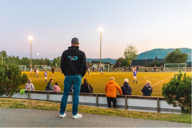 En elektriker står og ser utover en godt opplyst fotballbane på kveldstid