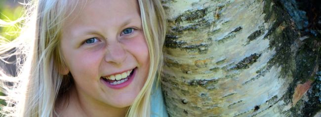 Jente smiler og holder rundt et tre