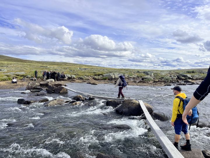 Plankeovergang ved en elv på fjellet med turgåere som tar seg over