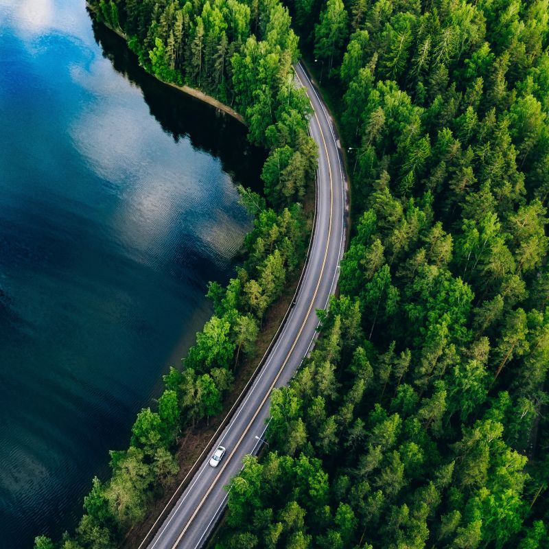 Overblikk over et vakkert landskap med skog og innsjø, med en bilvei i midten