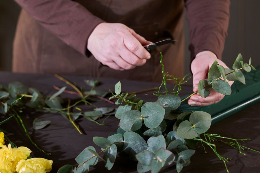 en blomsterdekoratør som lager bukett med eukalyptus