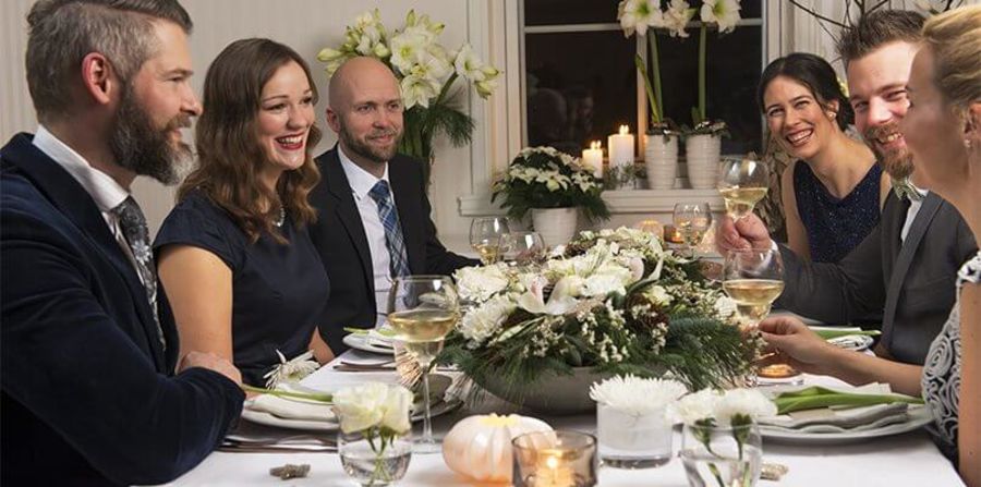 Selskapskledde mennesker rundt et spisebord med flott blomsterdekorasjon på