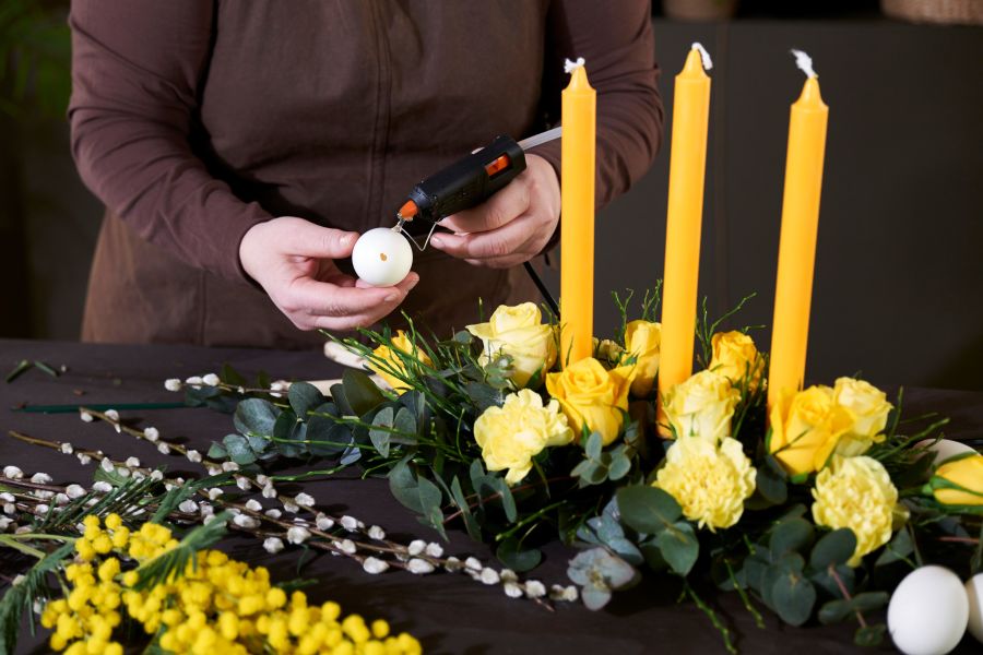 en blomsterdekoratør som lager bordpynt med eukalyptus, blomster og lys