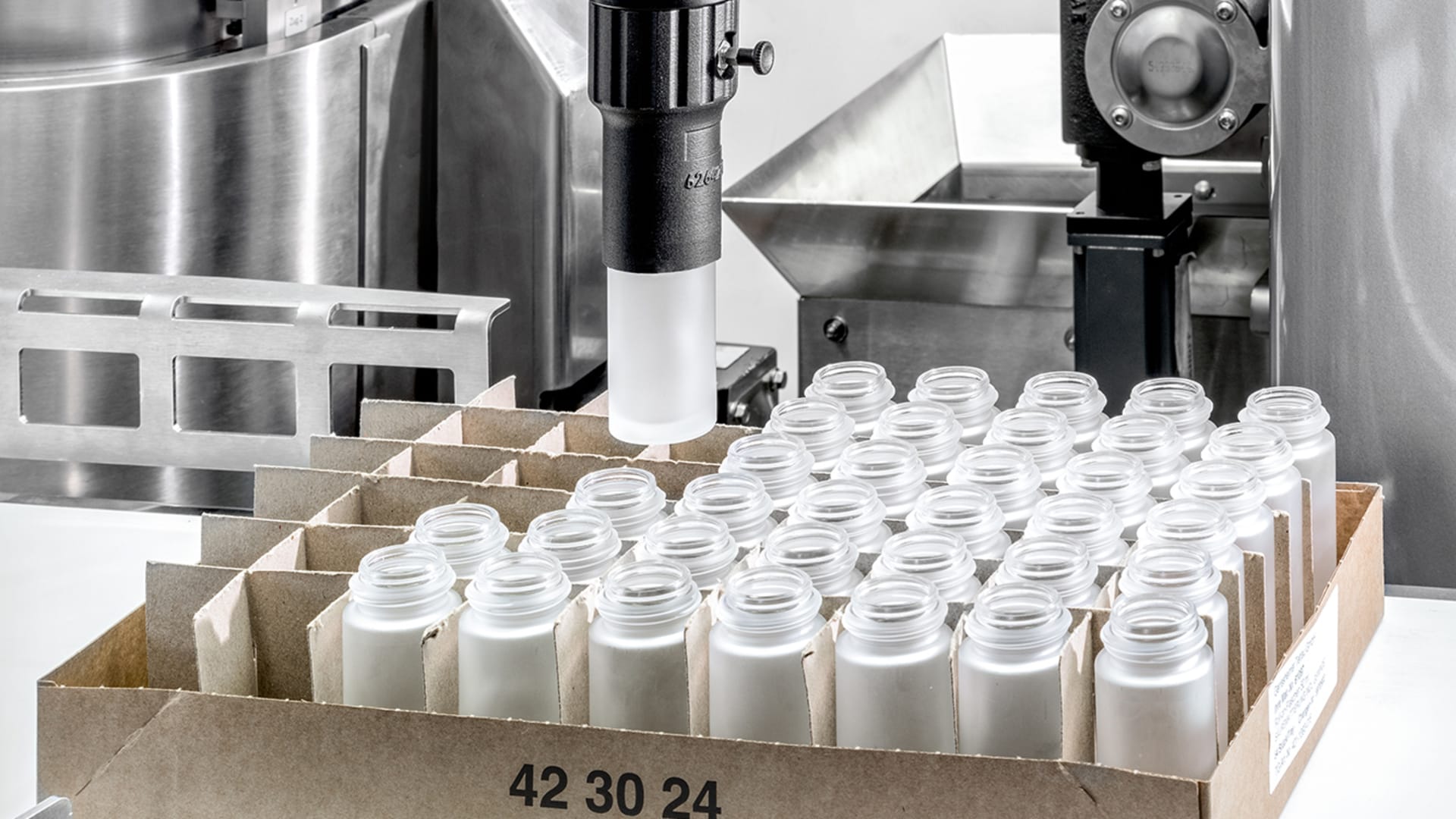 View of a box with cosmetic bottles. Above it is a cobot with a cosmetics bottle in its gripper arm.