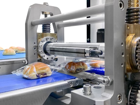 Madelaines freshly packed in tubular bags are placed in secondary packaging by robots