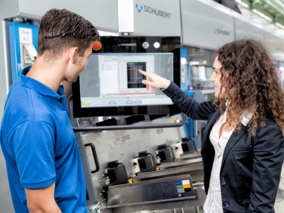 Two employees look at a machine dashboard