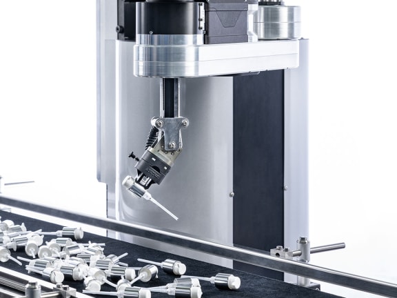 Der Cobot tog.519 über einem Transportband, auf dem kleine Pumpen liegen.