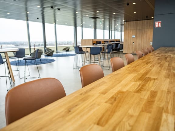 Langer Tisch aus Holz mit Stühlen. Im Hintergrund sind weitere Sitzinseln sichtbar.