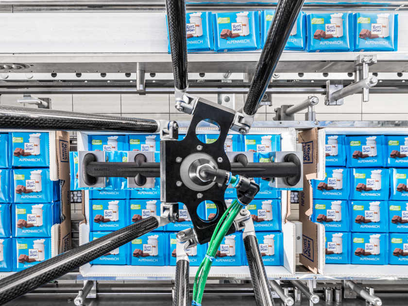 A robot places individual bars from transport cartons onto a feeding conveyor belt.