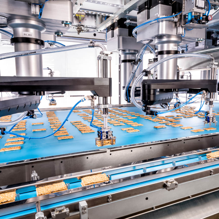 Several pick & place robots take flat biscuits from a conveyor, stack them and place them in a chain.