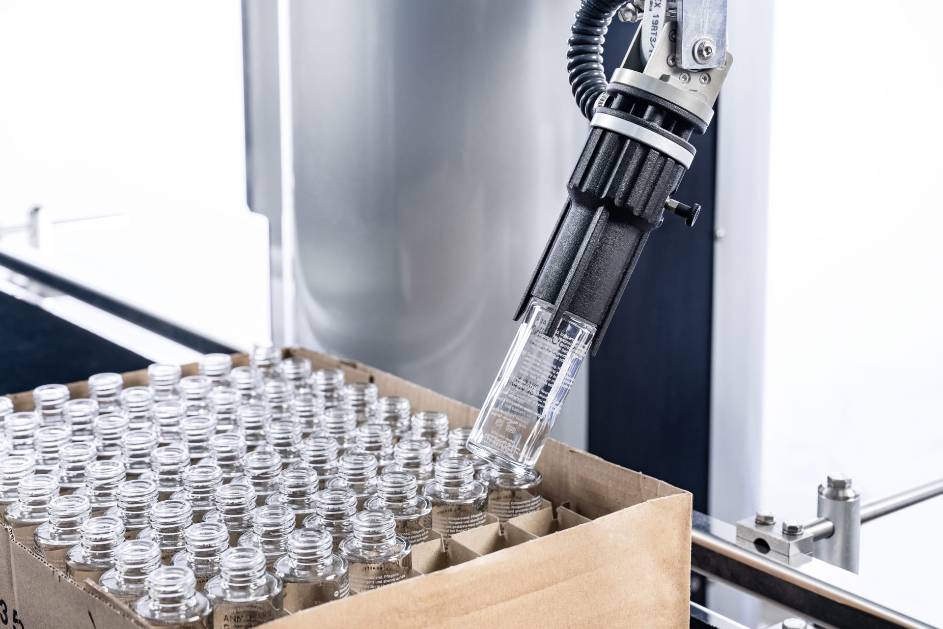 The cobot takes a glass bottle from a cardboard tray. 