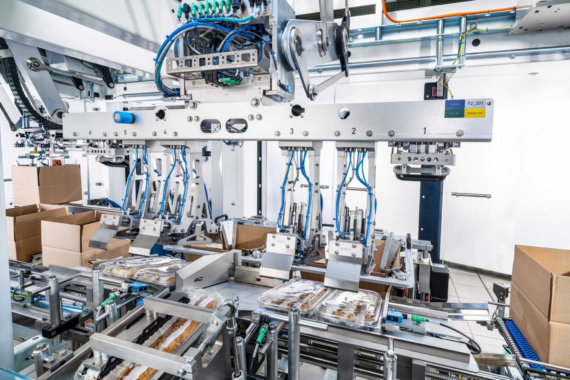 In a single line, coffee cakes that have been shrink-wrapped are picked up by a packaging robot and placed into boxes.