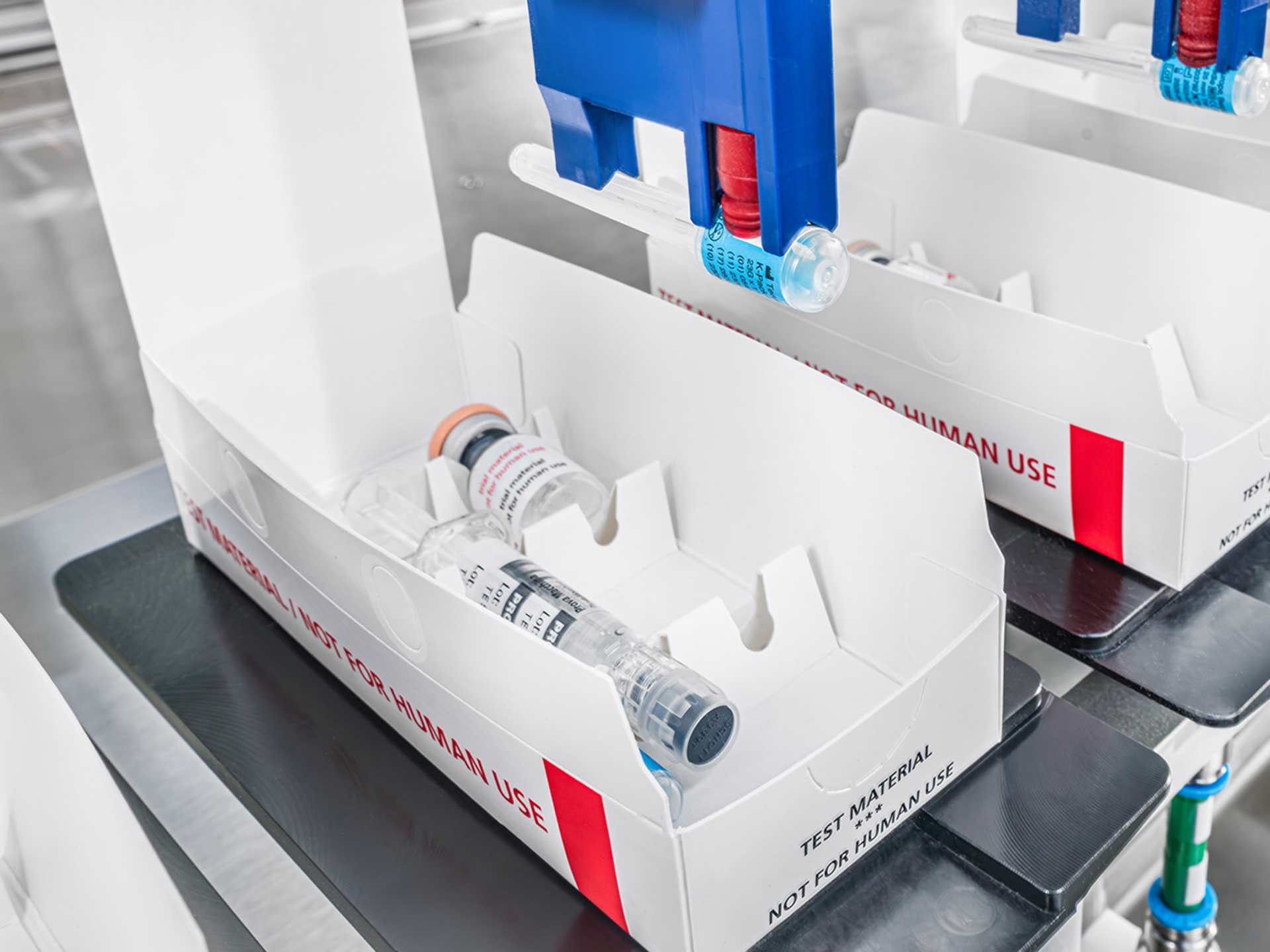 Ein Roboter legt eine Spritze in eine geöffnete Kartonschachtel.