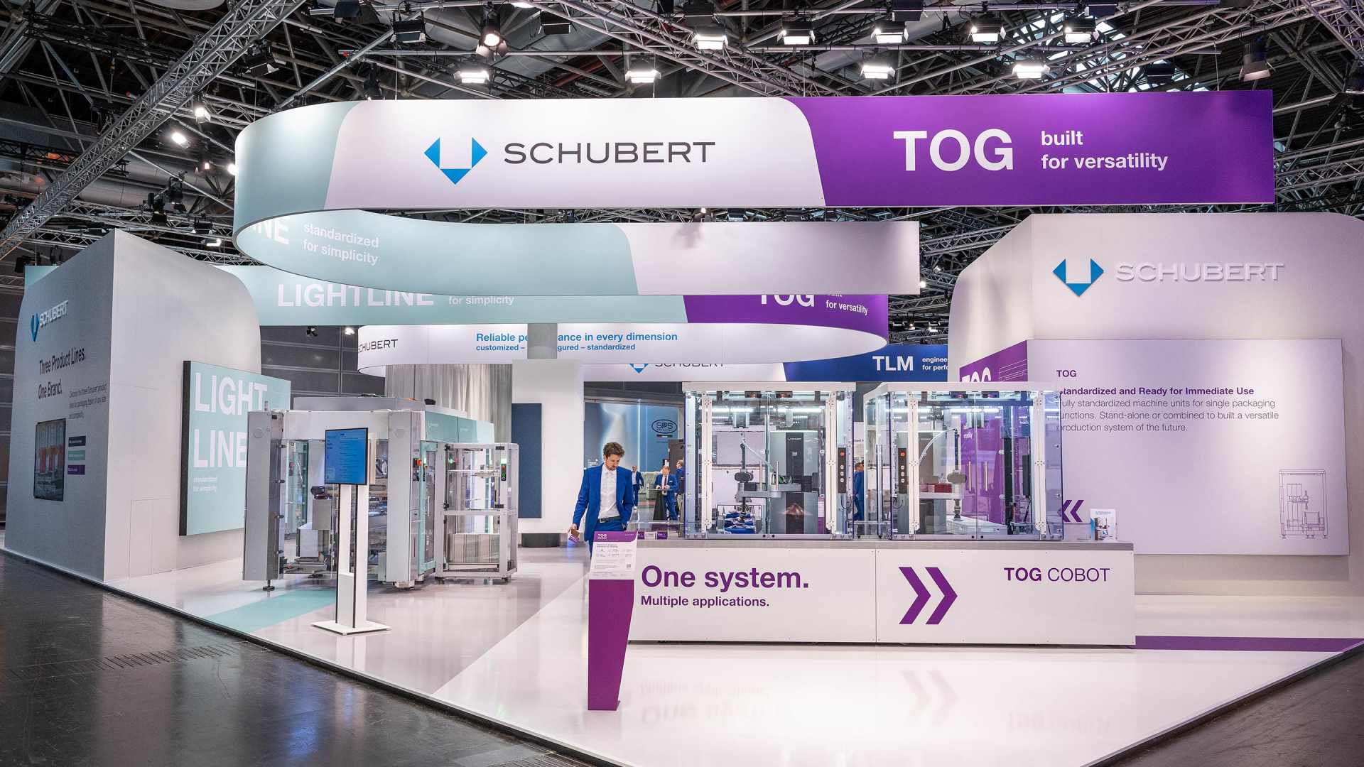 Schubert trade fair stand featuring several packaging machines and large-format brand banners at a trade fair.