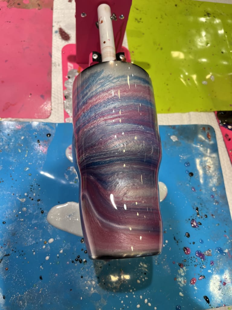 Pink, blue and silver galaxy-swirl resin tumbler drying on a turning stand at ATL Fluid Art in Brookhaven, Atlanta