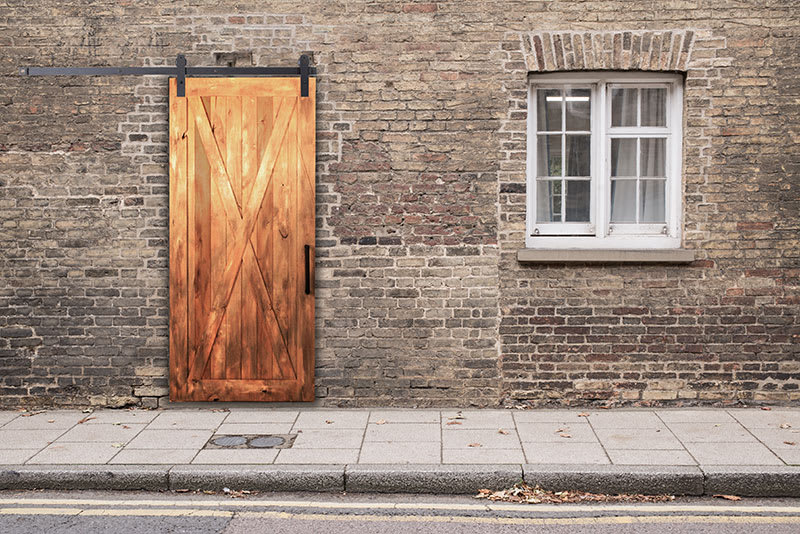 Cedar barn door with an X brace and black sliding hardware on a brick exterior wall.
