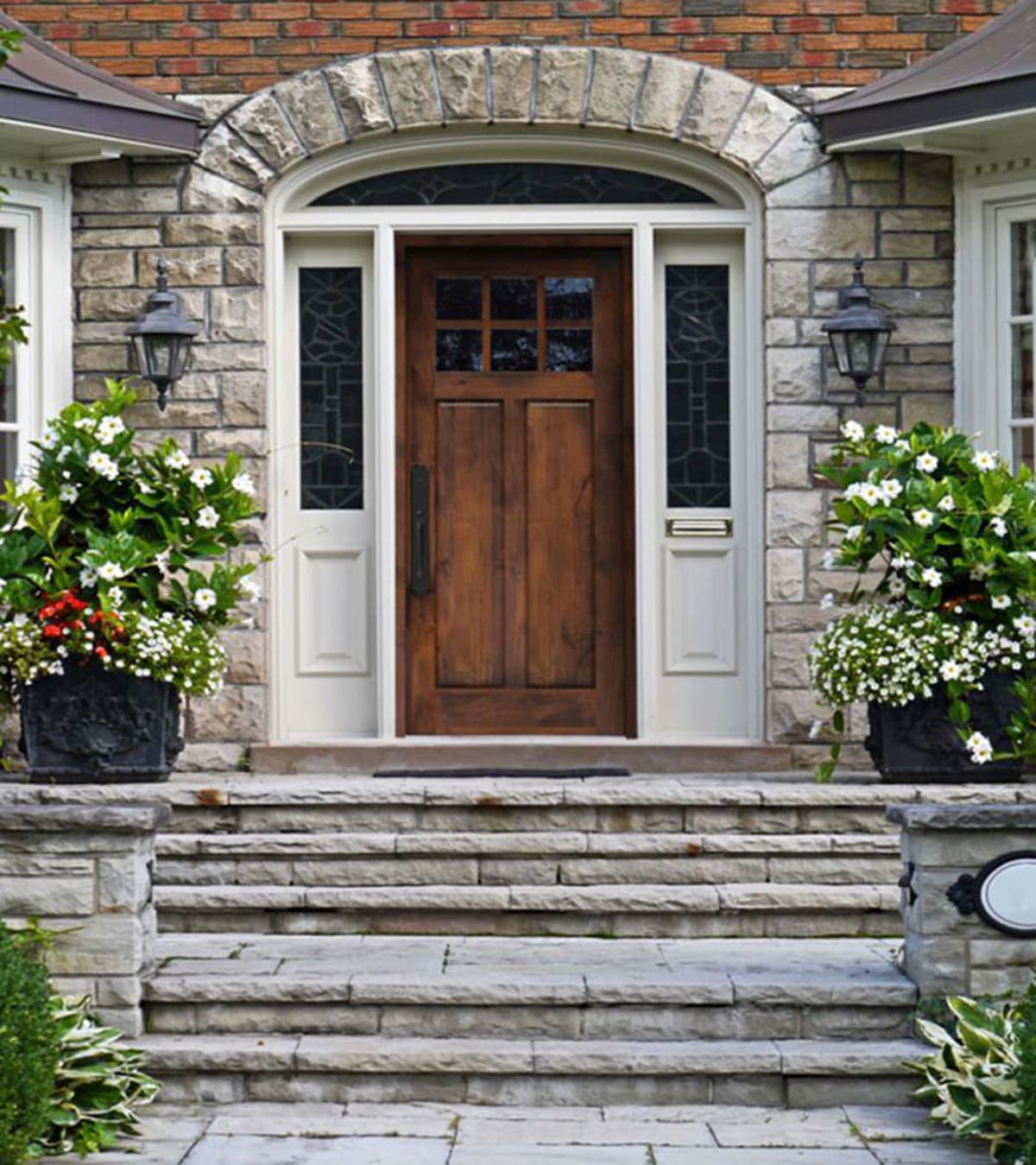 Wood front entry door with white sidelights, trim and a transom against a stone wall