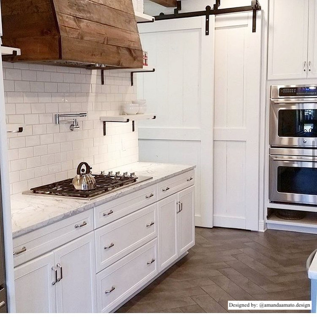 country chic farmhouse style kitchen with subway tile backsplash, wood stove vent, and white bypassing barn doors