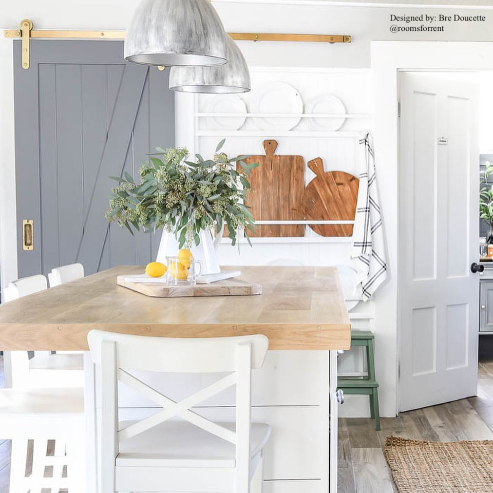 white and airy farmhouse style kitchen with butcher block counters and grey sliding bard door with brass hardware