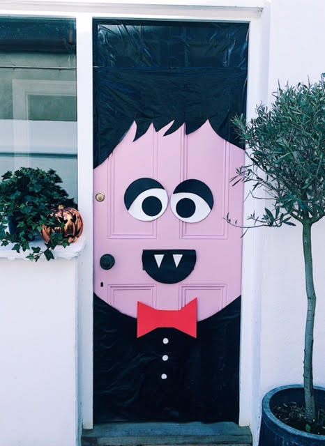 Pink front door dressed as Dracula with black hair and vest, white fangs and a red bow tie