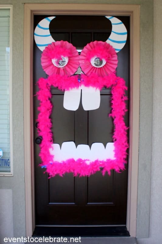 Front door monster with a bright pink feather boa mouth, large eyes and striped blue horns