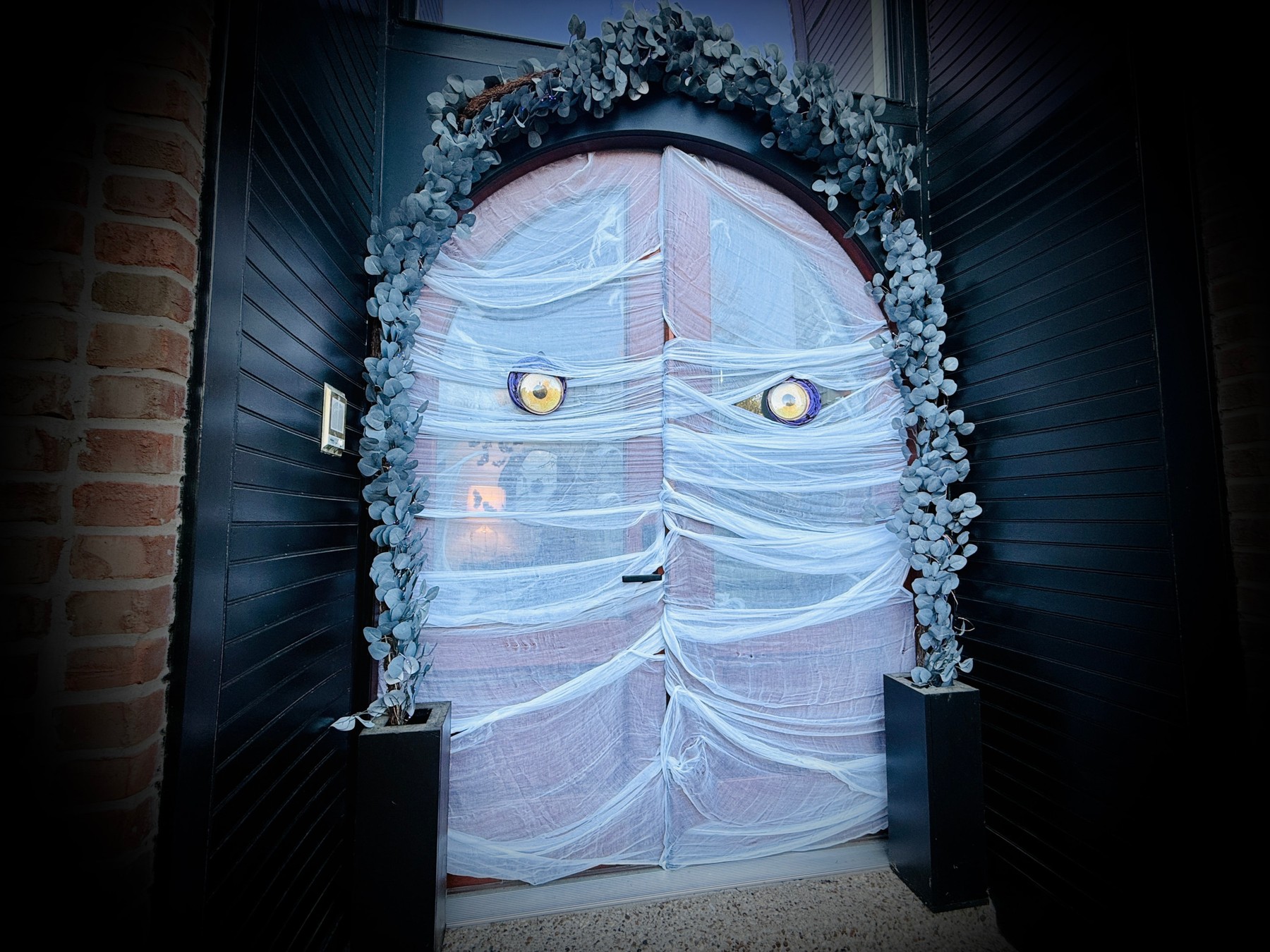 A pair of arched double front doors wrapped together as a mummy with two yellow eyes
