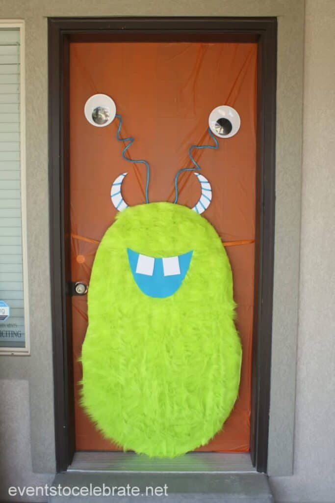 Green furry monster attached to a front door with a blue mouth and blue horns