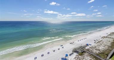 Stunning aerial view of pristine white sand beach with turquoise waters and beachside amenities including umbrellas and boardwalk access.