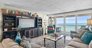 Sink into plush sofas while ocean waves dance beyond your floor-to-ceiling windows in this elegant beachfront living room.