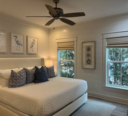 Spacious main floor king guest suite with soft lighting, artwork and natural light from window with blinds for privacy