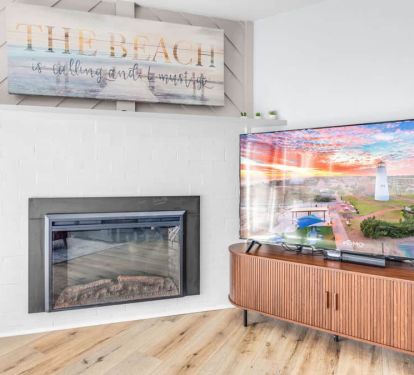 Electric fireplace with LED glow, &ldquo;The beach is calling&rdquo; art, and a 65&rdquo; TV for cozy nights.