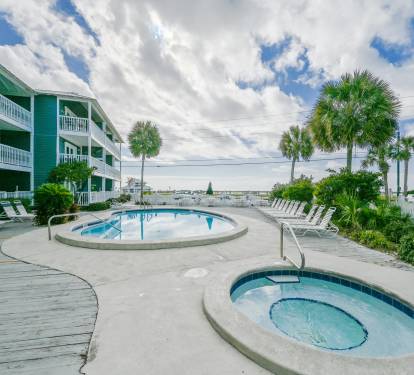 This picture shows the heated pool and hot tub located out the the patio gate of our beach condo. The pool is surrounded by a deck with lounge chairs, while the hot tub is tucked away in the corner. The crystal clear blue water sparkles in the sun, and th