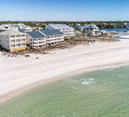 Aerial view of gulf front vacation rental properties situated directly on pristine white sand beach with crystal-clear emerald waters.