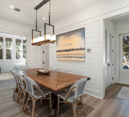 Gather around this stunning dining table where coastal artwork and warm lighting create the perfect setting for your memorable meals together.