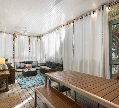 Your private screened porch invites you to unwind with plush seating, soft lighting, and peaceful garden views beyond flowing curtains.