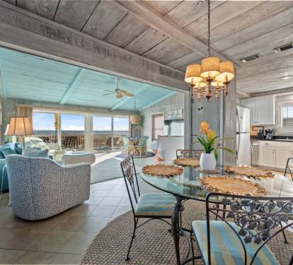 Step into your coastal retreat where rustic charm meets ocean elegance. Dine under warm chandelier light while waves beckon beyond floor-to-ceiling windows.
