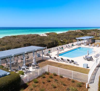 Beachfront property featuring elevated pool deck with pristine white sand beach and turquoise waters beyond natural dune vegetation.