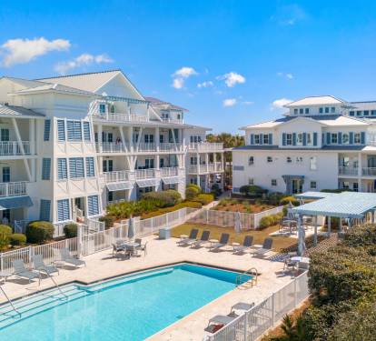 Coastal vacation buildings with swimming pool and outdoor spaces surrounded by tropical landscaping under bright blue skies.