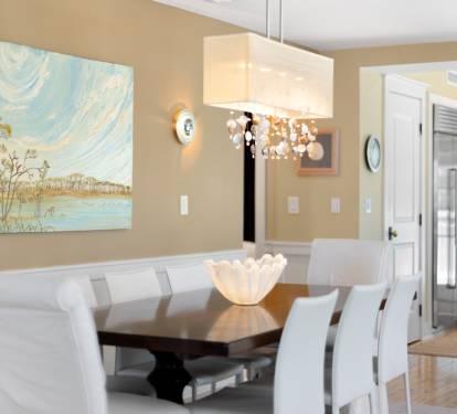 Gather around this elegant dining table for memorable meals, bathed in warm chandelier light with coastal artwork setting the scene.