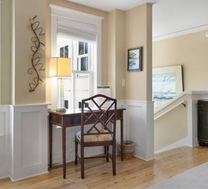 Settle into your charming writing nook with coastal artwork and warm natural light streaming through windows.
