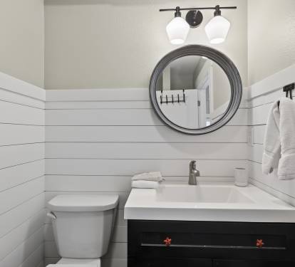 Your pristine powder room features modern farmhouse charm with crisp white shiplap walls, elegant lighting, and thoughtful amenities.