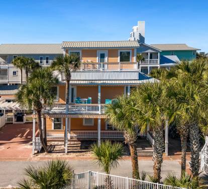 Coastal retreat featuring vibrant yellow beach house with multiple balconies surrounded by swaying palms and neighboring beach homes.