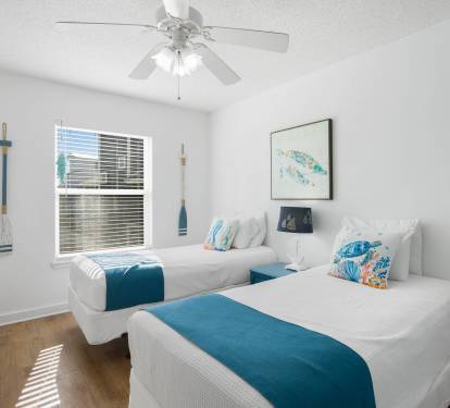 Drift off to sleep in this bright coastal bedroom with twin beds, nautical touches, and gentle ceiling fan breeze.