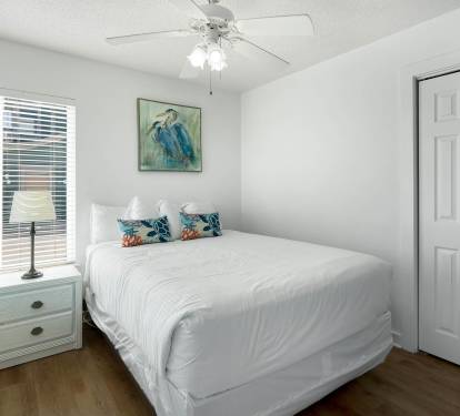 Drift into peaceful sleep in your bright bedroom, complete with fresh linens, tropical artwork, and gentle ceiling fan for perfect comfort.